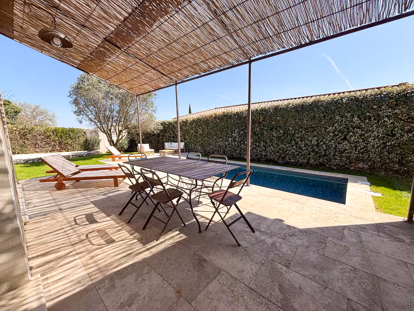 Grande table sous la pergola de canisse, face à la piscine